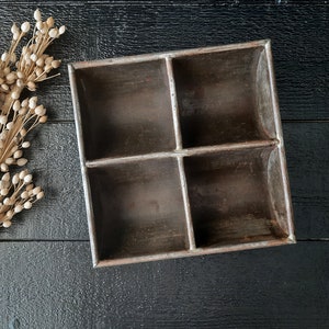 Puede incluir: Una caja de madera rústica con cuatro compartimentos. La caja está hecha de madera oscura y tiene un acabado desgastado. Es perfecta para guardar objetos pequeños, como joyas, monedas u otras chucherías.