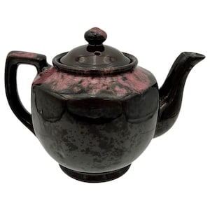 May include: A ceramic teapot with a dark brown base and a speckled, reddish-purple upper section. The teapot has a curved handle, a spout, and a lid with a small knob. The glossy finish gives the teapot a vintage look.