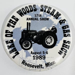 Puede incluir: Un botón redondo con un tractor negro sobre un fondo de mapa azul claro. El texto dice "Lake of the Woods Steam & Gas Show", "17th Annual Show", la fecha "5-6 de agosto de 1989" y el lugar "Roosevelt, Minn."