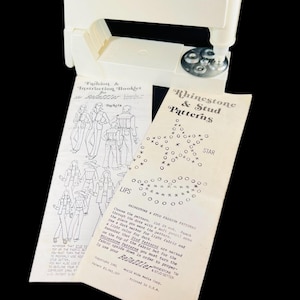 May include: A vintage white BeDazzler tool with instruction booklets. The booklets feature fashion illustrations and rhinestone and stud patterns. The text on the booklet reads "Rhinestone & Stud Patterns" and "Fashion & Instruction Booklet for the BeDazzler".