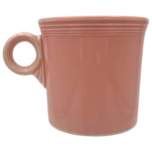 Puede incluir: Una taza de cerámica de color rosa coral sólido con un cuerpo cilíndrico y tres anillos horizontales en relieve cerca del borde superior. La taza incluye un asa circular unida al lateral con una base ensanchada, mostrando un acabado liso y brillante.