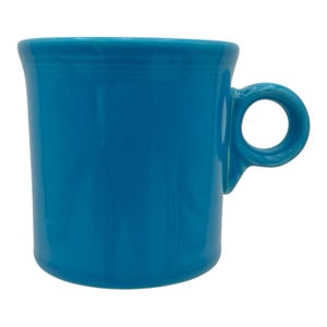 May include: A solid turquoise ceramic mug with a smooth, glossy finish. The mug features a cylindrical body with a slightly flared rim and a small, circular handle attached to the side. The design is simple, featuring a uniform colour throughout.