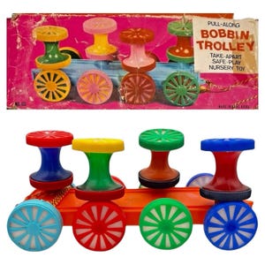 May include: A vintage pull-along toy train with colorful bobbins and wheels. The toy features a variety of colors, including red, yellow, green, and blue. The packaging reads "PULL-ALONG BOBBIN TROLLEY TAKE-APART SAFE-PLAY NURSERY TOY."