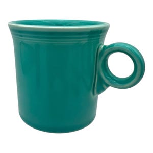 Op de afbeelding: Een effen, groenblauwe keramische mok met een glanzende afwerking, voorzien van een cilindrisch lichaam, een brede rand met een subtiel horizontaal ringdetail en een cirkelvormig handvat aan de zijkant. De mok heeft een egale kleur.