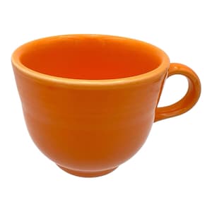 May include: A vibrant orange ceramic teacup with a rounded body and a curved handle. The cup has a glossy finish and a smooth rim. The interior of the cup is the same bright orange color.