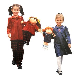 May include: Two dolls with yarn hair and round faces. One doll wears a red long-sleeved top with a collar and dark plaid pants. The other doll wears a navy blue dress with a white collar and white patterned tights, holding a smaller doll.
