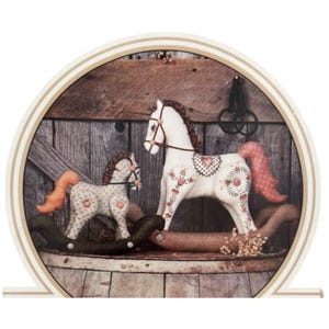 May include: Two fabric rocking horses in a circular frame. The larger horse is white with red heart patterns and a pink tail. The smaller horse is grey with a floral pattern and an orange tail. Both have dark brown rockers and brown bridles.