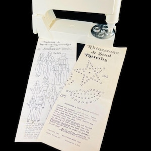 May include: A white plastic tool for applying rhinestones and studs to fabric. The tool is shown with a booklet of patterns for stars, lips, and jackets. The booklet includes instructions for using the tool and the text "Rhinestone & Stud Patterns".