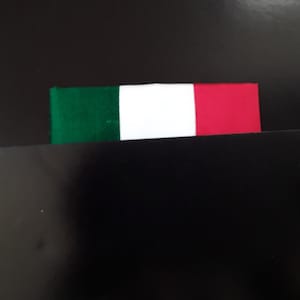 May include: A small Italian flag with green, white, and red stripes is partially visible on a black surface.