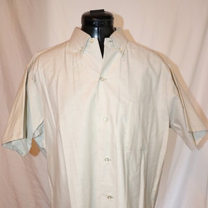 Pode incluir: Uma camisa de manga curta bege claro com botões e um bolso no peito.