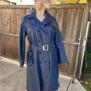 May include: A navy blue long-sleeved trench coat with a double-breasted closure, a belt, and two flap pockets.