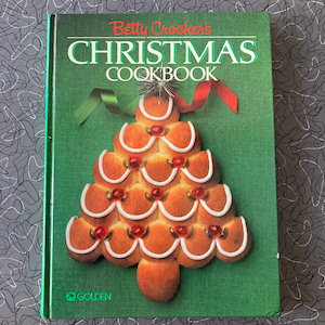 以下が含まれることがあります： 「Betty Crocker's Christmas Cookbook」というタイトルの緑色のハードカバーの料理本。表紙にはジンジャーブレッドのクリスマスツリーの絵が描かれている。この本はゴールデン社から出版されている。