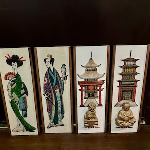 May include: Four framed wall art panels with Japanese-themed designs. The panels depict geishas, pagodas, and a seated Buddha. The geishas wear colorful kimonos. The pagodas and Buddha are in shades of red, gold, and brown.