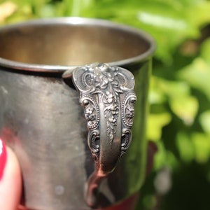 May include: A silver cup with an ornate handle. The handle is decorated with a floral design.