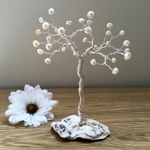 May include: A white pearl wire tree sculpture with a twisted wire trunk and branches. The tree is sitting on a white seashell base.