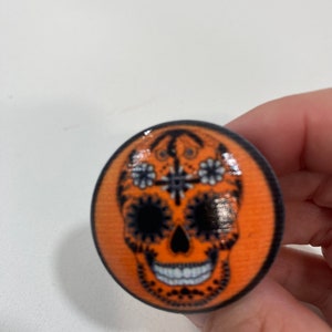 May include: Orange and black sugar skull design on a round, wooden knob.