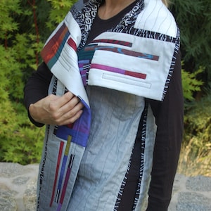 Peut inclure: Un gilet matelassé gris et blanc avec une bordure à motifs noirs et blancs. Le gilet a un grand col rabattu et un design géométrique unique sur le devant.