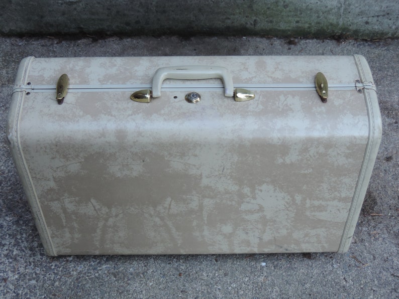 May include: Vintage beige suitcase with a speckled pattern, a cream-colored handle, and gold-toned metal accents. The suitcase has a rectangular shape and is designed for travel.