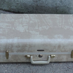 May include: Tan vintage suitcase with a textured pattern and gold-colored hardware. The suitcase has a handle and a lock. The corners are reinforced with white trim. A classic travel accessory.