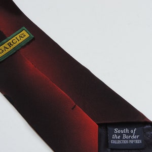 May include: A black and red tie with a gradient pattern. The tie has a label that says "J. Garcia" and another label that says "South of the Border Collection Fifteen".
