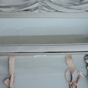 May include: Open vintage suitcase with a light green interior and exterior. The suitcase has a metal frame and hinges. Beige fabric straps and a key are visible inside. The interior has a pleated fabric detail.