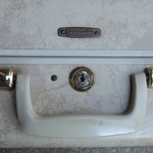 May include: Close-up of a vintage Samsonite suitcase. The suitcase has a cream-colored exterior with a speckled pattern. It features a brass lock, handle, and accents. The Samsonite logo is visible.