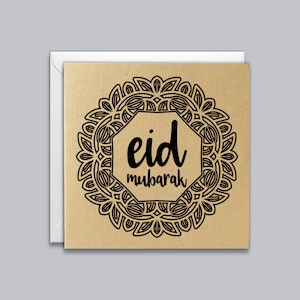 May include: Square greeting card with a kraft paper texture, featuring a black ornamental design around the text "eid mubarak." The card is inside a white envelope. The design is centered on the card.