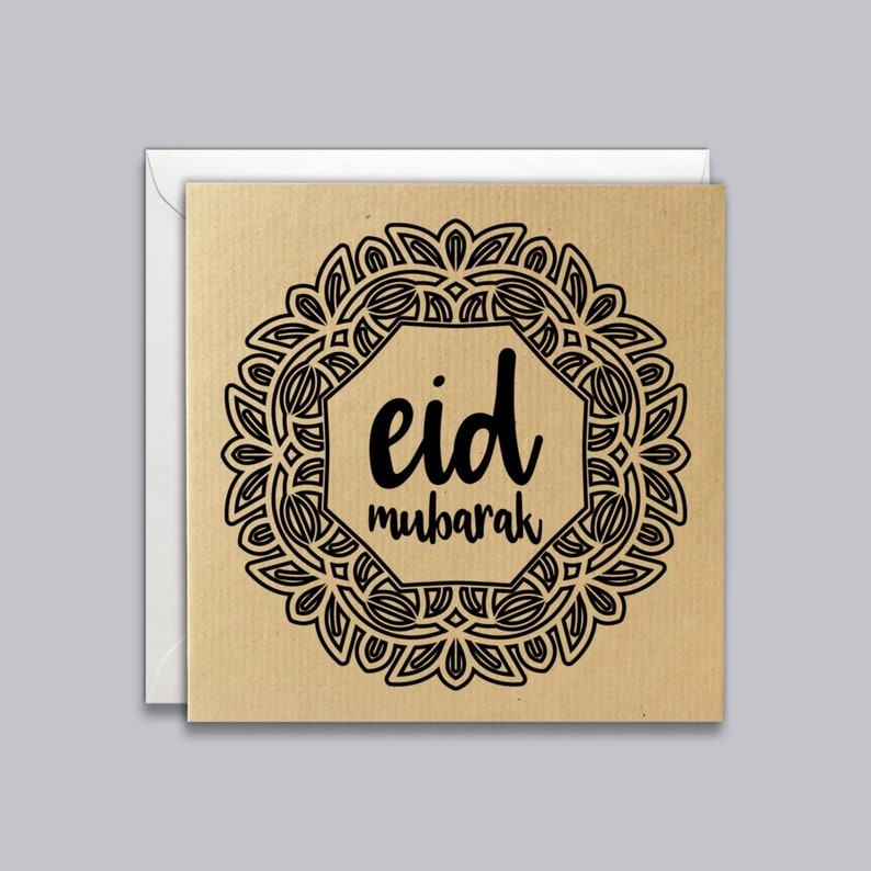 May include: Square greeting card with a kraft paper texture, featuring a black ornamental design around the text "eid mubarak." The card is inside a white envelope. The design is centered on the card.