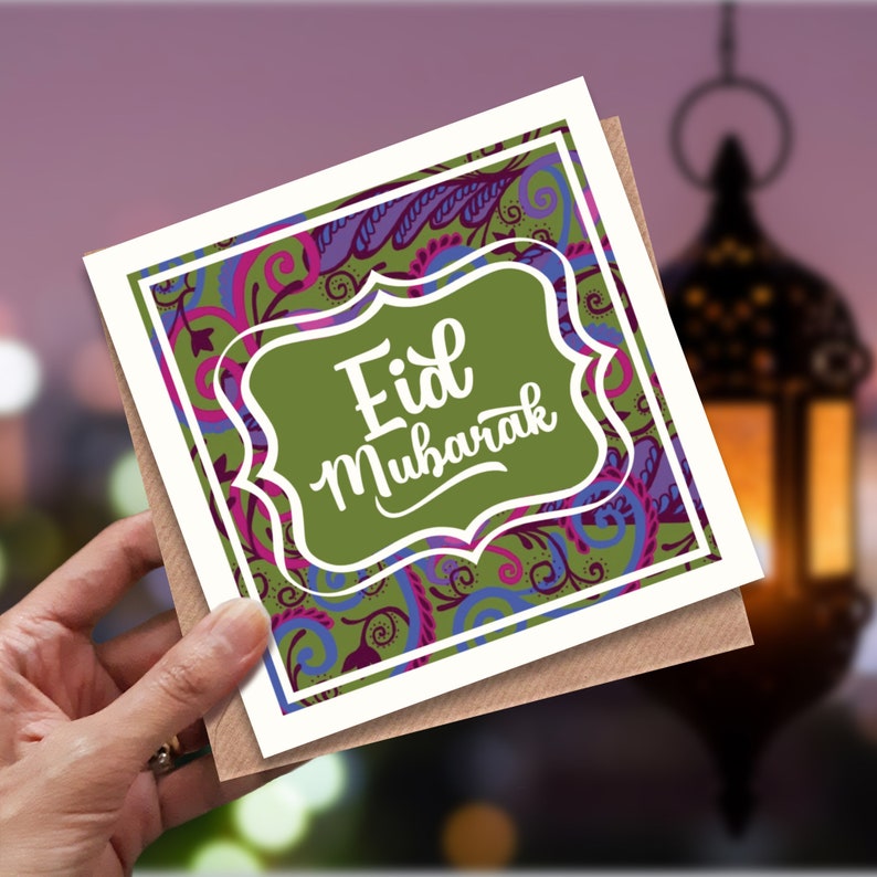 May include: A white card with a green, purple, and pink floral design. The card has a green frame with the text "Eid Mubarak" in white.