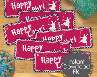 May include: Six pink gift tags with a white border and white text that reads "Happy Lohri". Each tag features a white silhouette of a person dancing with a stick. The tags are on a wooden surface with a blue and gold patterned fabric in the background.