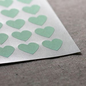 May include: A sheet of white paper with a pattern of light green heart stickers.