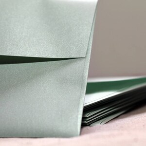 May include: A stack of light green envelopes with a single envelope standing upright in front of the stack.