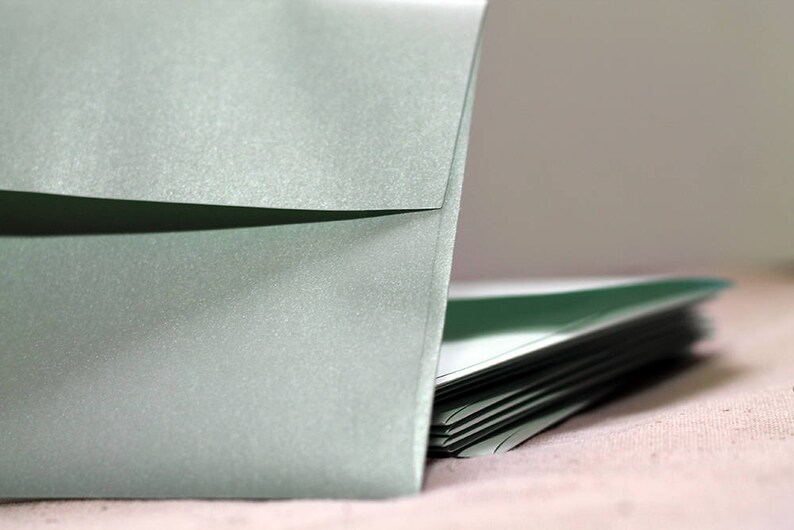 May include: A stack of light green envelopes with a single envelope standing upright in front of the stack.