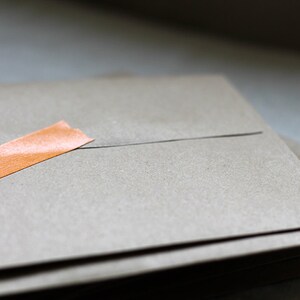 May include: A stack of brown envelopes with a single orange piece of tape on the top envelope.