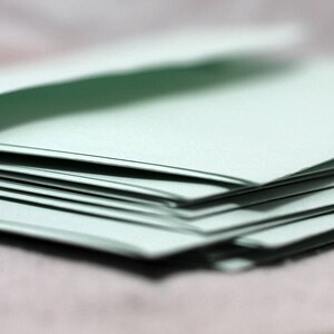 May include: A stack of light green paper envelopes, folded and ready to be mailed.