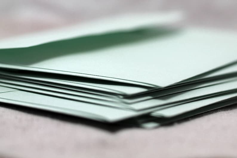 May include: A stack of light green paper envelopes, folded and ready to be mailed.