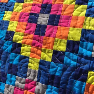 May include: A colorful quilt with a patchwork design featuring squares of blue, green, orange, pink, and gray fabric. The quilt is quilted with a circular pattern.