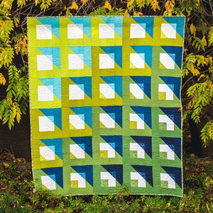 Puede incluir: Una colcha con un patrón geométrico en tonos de azul, verde y blanco. La colcha está compuesta por cuadrados y triángulos, y los colores están dispuestos en un degradado.