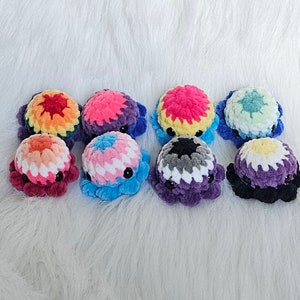 May include: Eight crocheted octopus plushies in various colors, including rainbow, purple, blue, and green. Each octopus has a white crocheted face with black eyes.