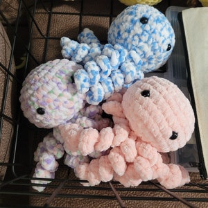May include: Three crocheted octopus plushies in a wire basket. One is blue and white, one is pink, and one is purple and white.
