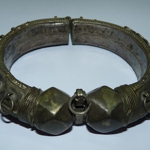 May include: A silver and brass bangle bracelet with decorative details and a hinged clasp. The bracelet has a series of small loops along the sides.