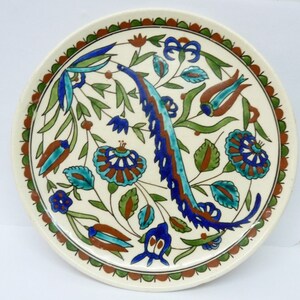 Puede incluir: Un plato de cerámica blanco con un diseño floral azul, verde y marrón. El plato tiene un borde decorativo.