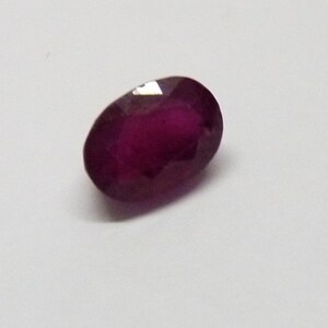 May include: A deep red oval gemstone with a smooth, polished surface.