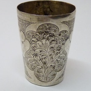 Könnte beinhalten: Eine silberne Tasse mit einem aufwendigen floralen Design, das in die Oberfläche graviert ist. Das Design zeigt eine große Blume, die von kleineren Blumen und Blättern umgeben ist.
