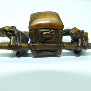 Puede incluir: Una pequeña escultura de madera de un palanquin llevado por dos ratones. El palanquin está decorado con intrincados tallados y los ratones están representados en posición sentada.