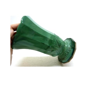 May include: A green ceramic vase with a flared top and a detailed floral design near the base. The vase has a glossy finish and is held by a hand against a white background. The vase is approximately 20 cm tall.