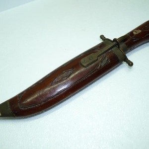 May include: A wooden-handled knife with a brass sheath and a carved wooden handle. The sheath has a brass latch and a decorative design.
