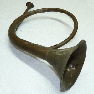 May include: A vintage brass hunting horn with a curved design and flared bell. The horn has a tarnished, aged appearance, suggesting it is an antique musical instrument. The mouthpiece is small and circular.