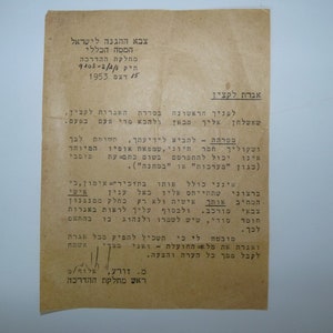 以下が含まれることがあります： ヘブライ語のテキストが書かれた白黒の文書。文書のタイトルは「将校へのメッセージ」で、1953年と日付が記されています。テキストは、情報の機密保持とトレーニング目的での使用の重要性について述べています。