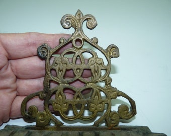 May include: A gold metal bookend with an intricate design of swirling lines and leaves. The bookend is made of a single piece of metal and has a decorative top.